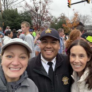Two women and a male police officer smile for the camera with a crowded street in the background.